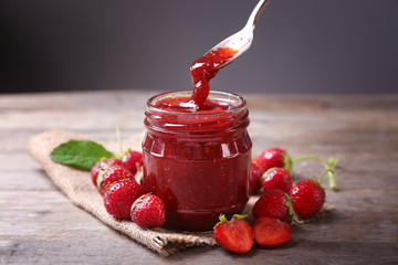 Glass jar and spoon with delicious strawberry jam on wooden table - obrazy, fototapety, plakaty