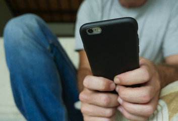 hands of young man holding mobile phone sitting relaxed at home sofa couch using internet social media app on smartphone networking and texting