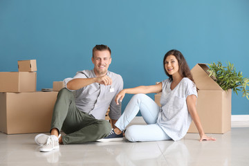 Happy young couple with key from their new house and moving boxes sitting on floor indoors