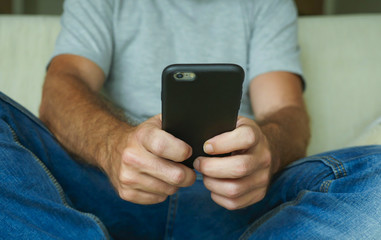 hands of young man holding mobile phone sitting relaxed at home sofa couch using internet social media app on smartphone networking and texting