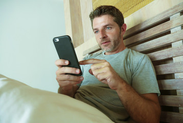lifestyle indoors portrait of young happy and attractive man at home bedroom using internet social media app networking from bed thoughtful and relaxed