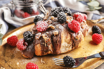 Tasty croissant with chocolate paste, nuts and berries on metal tray