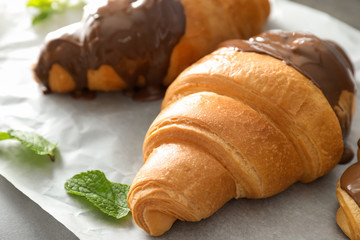 Tasty croissant with chocolate sauce on parchment, closeup