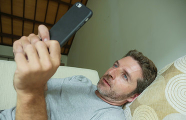 Fototapeta premium lifestyle indoors portrait of young happy and attractive man at home sofa couch using internet social media app on mobile phone networking relaxed
