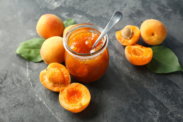 Jar with delicious apricot jam and fresh fruit on grunge table