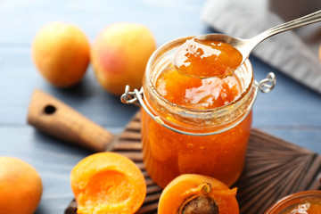 Spoon with delicious apricot jam over jar, closeup