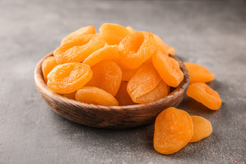Bowl with dried apricots on grey background