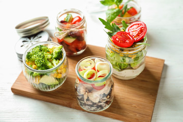 Delicious vegetable salads with chicken in mason jars on wooden board