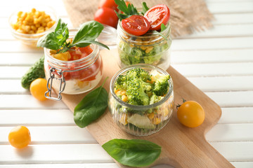 Delicious vegetable salads in mason jars on wooden board
