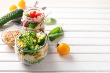 Delicious vegetable salads in mason jars on white table
