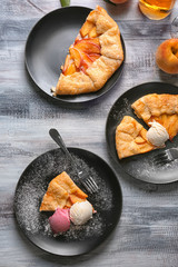 Plates with pieces of delicious peach galette and ice-cream on wooden table