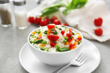 Bowl with tasty boiled rice and vegetables on grey textured table