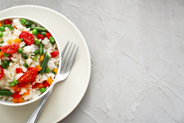 Bowl with tasty boiled rice and vegetables on grey textured table