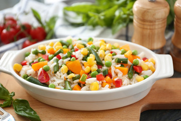 Dish with tasty boiled rice and vegetables on wooden board