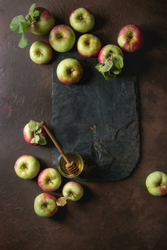 Ripe organic gardening green red apples with leaves and jar of honey on black slate board over dark texture background. Flat lay, space. Autumn harvest.