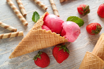 Waffle cone with delicious strawberry ice-cream and sticks on wooden background