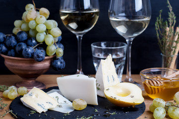 Cheese plate served with wine, grapes, honey and pear on a dark background