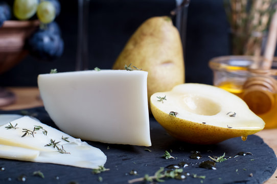 Cheese plate served with grapes, honey and pear on a dark background
