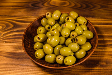 Ceramic plate with green olives on wooden table
