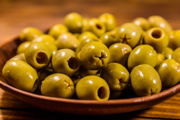 Ceramic plate with green olives on wooden table