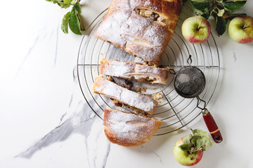 Homemade sliced puff pastry apple strudel pie on cooling rack served with ripe fresh apples,...