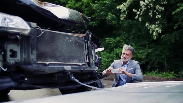 Mature man taking pictures of a broken car after an accident.