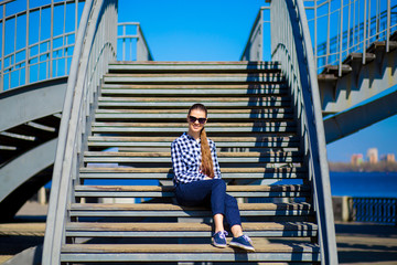 Young stylish woman sits on street stairs in sunny day. Street style