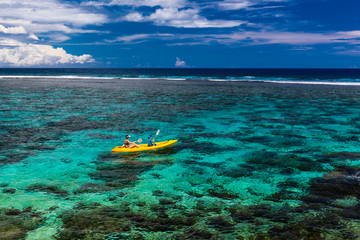 Female and little boy paddling canoe on a lagoon with coral reef.