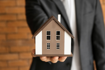 Real estate agent with house model near brick wall, closeup. Mortgage concept