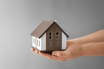 Fototapeta na wymiar Man holding house model on grey background. Mortgage concept