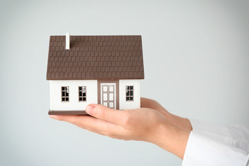 Real estate agent with house model on light background, closeup