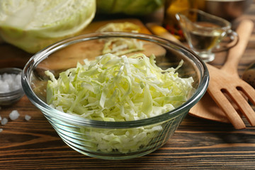Bowl with cut cabbage on wooden table, closeup