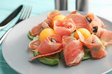 Delicious melon balls with prosciutto and olives on plate, closeup