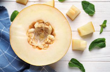 Half of ripe melon with pieces on white wooden table