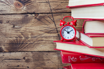 A stack of hardcover books and an alarm clock on a wooden table. Copy space for text