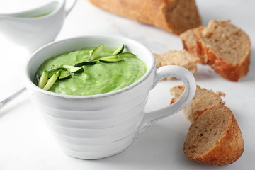 Tasty zucchini soup in cup with bread on light table