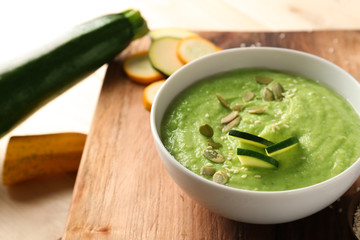 Tasty zucchini soup in bowl on wooden board
