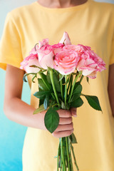 Woman holding bouquet of beautiful roses on color background, closeup