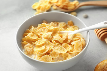 Bowl with healthy cornflakes and milk on light table, closeup