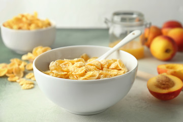 Bowl with healthy cornflakes, milk and peaches on light table, closeup