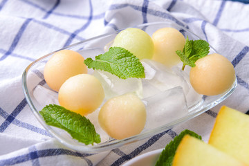Plate with fresh melon balls and ice cubes on table