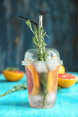 Fresh grapefruit cocktail with rosemary in plastic cup on color table