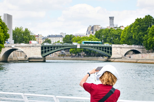 A woman in a red T-shirt takes pictures of a beautiful bridge over the river Seine, Paris, France. View from the back. Tourist on the boat deck