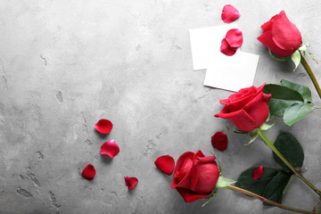 Beautiful red roses and blank cards on grey background