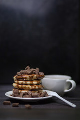 Freshly baked, tender punkeyki soaked in chocolate sauce with pieces of milk chocolate. With a Cup of coffee. On dark background.