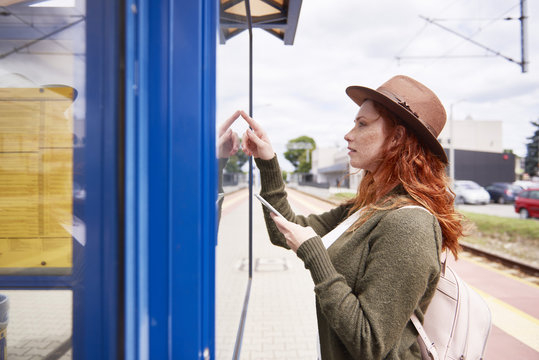 Redheaded young woman looking at timetable on platform