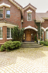 A welcoming entryway with ornamented wooden door, side windows and evergreens in a red brick...