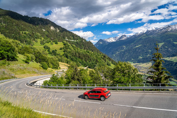 Red car on a road through switzerland alps. Curvy road in mountains. Traveling concept background.