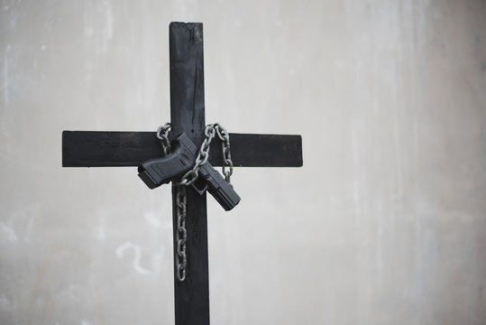 Black cross with chain and handgun on white grunge wall. Object and weapon concept. Christian religion theme. Halloween and criminal theme. Copy space on right.