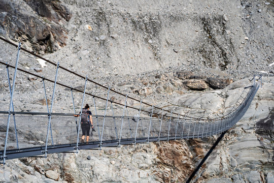 Female hiker walking on the hanging bridge over the Glacier de Corbassiere on a mountain trail around Valais Swiss Alps.